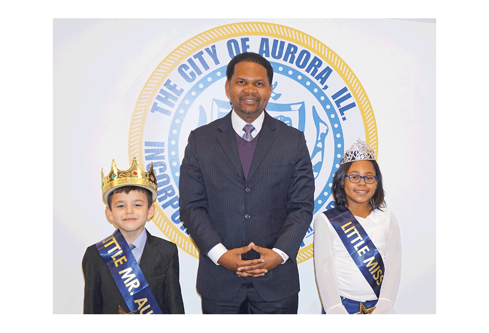 Mayor Richard C. Irvin of Aurora poses with Little Mr. Aurora, Benjamin Mendoza of Boulder Hill Elementary, and Alaria Selmon of Allen Elementary, Little Miss Aurora, at the Aurora City Council meeting Tuesday. Jason Crane/The Voice