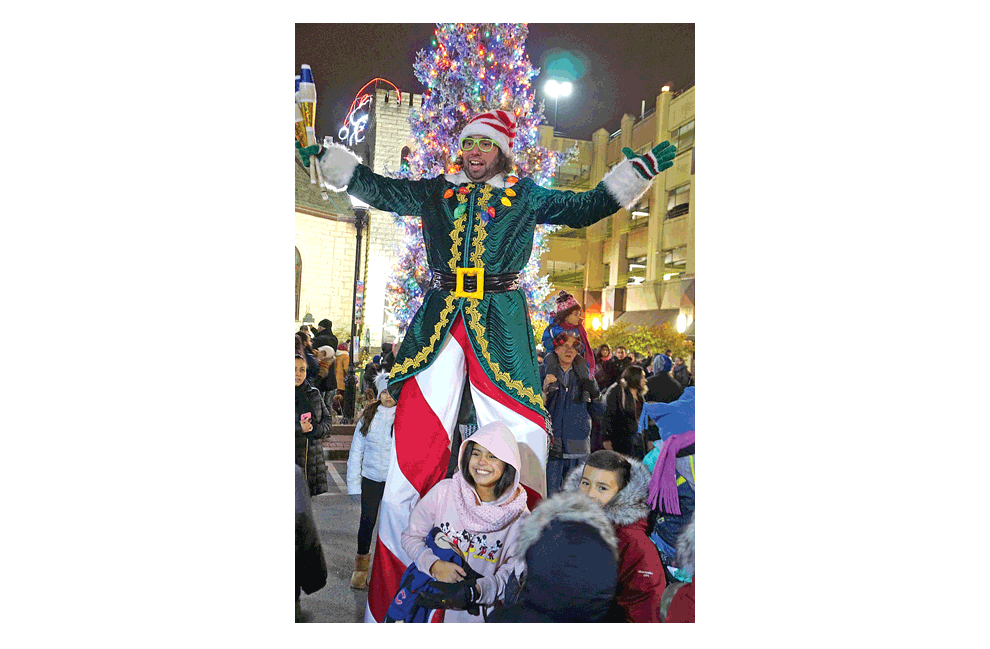 The world’s tallest elf is Jason Kullom at the Winter Lights in Aurora Friday to turn on the Christmas lights. Behind Kullom, is Santa peering over the top of the GAR building. See page 13 and facebook.com/thevoice.us. Jason Crane/The Voice