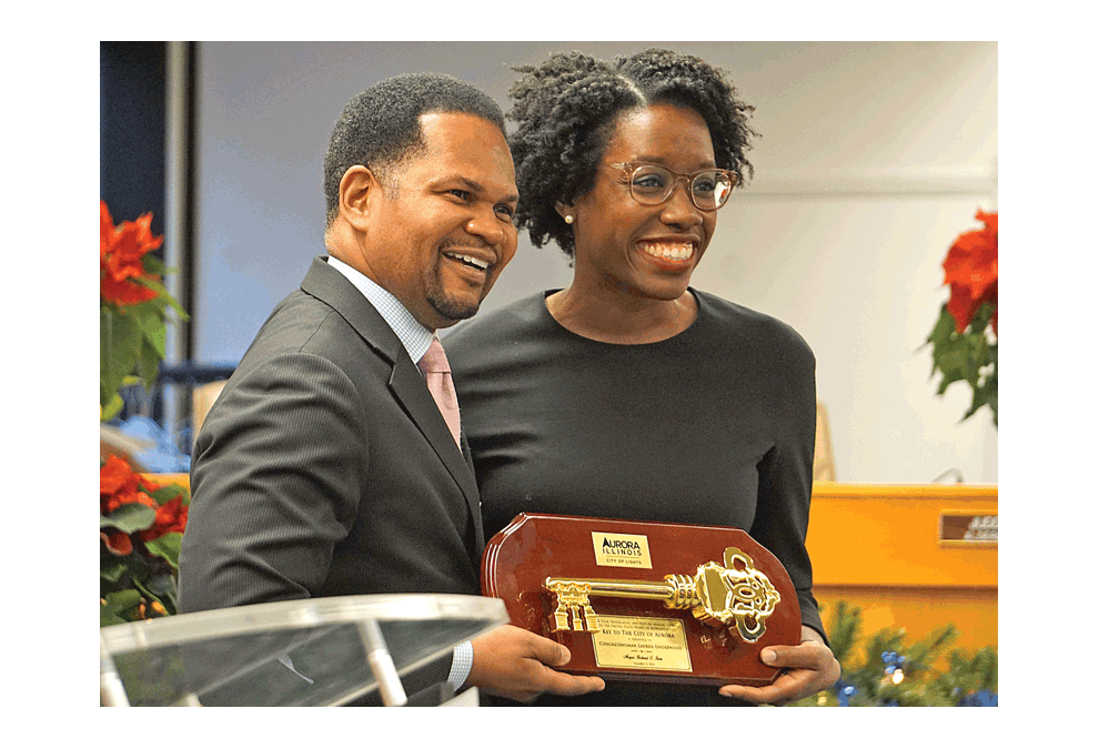 Mayor Richard C. Irvin of Aurora presents a Key to the City to and poses with congresswoman-elect Lauren Underwood of Naperville in a meeting Wednesday, Dec. 12 in the Aurora City Hall. Underwood was elected to the U.S. House of Representatives in the 14th District by defeating incumbent Randy Hultgren in the November 6 election. The short presentation included a few remarks by each person. She will take office after the first of the year in 2019. In attendance were high school girls from East Aurora, Metea Valley, and West Aurora High Schools. The proceedings were delayed nearly an hour following a nationwide bomb threat hoax. The City Hall building was evacuated. Police called the threat an E-mail phishing scam. It reached The Voice communities to include Aurora and Elgin. Carter Crane/The Voice