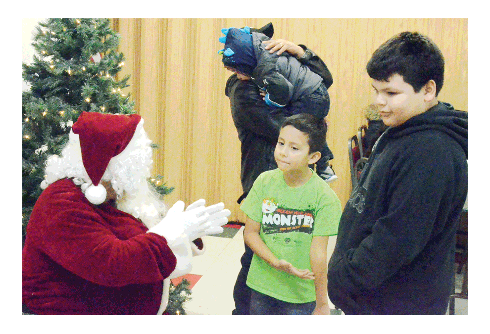 Aurorans Angel Velasquez, 6, and Aldo Sanchez-Mata, 9, visit with a sign-language Santa, December 11 at the 12th annual holiday party for hearing-impaired kids at Luigi’s Pizza in Aurora. Approximately 80 students, caregivers and teachers from West Aurora School District 129 and East Aurora School District 131 were guests of Aurora Noon Lions Club. Al Benson/The Voice