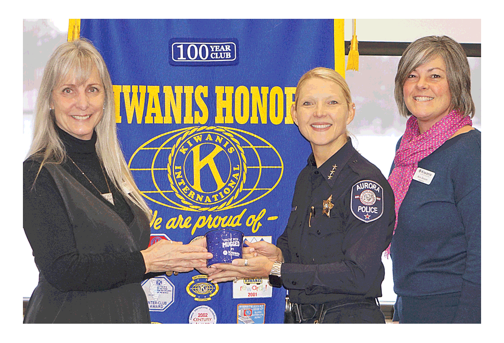 Kiwanis Club of Aurora member Amy Roth, left, hands a Kiwanis coffee mug to Aurora Police Chief Kristen Ziman at the Kiwanis Club meeting Tuesday at the Prisco Center in Aurora. Chief Ziman shared this year’s Police Department initiatives. Aurora has the second largest municipal police department with a budget of $73 Million and has 301 sworn officers, an increase from 289 recently, including four police dogs, 73 full-time non-sworn officers in telecommunications, booking, and records, and 33 part-time non-sworn employees. Chief Ziman said work is in focus to address a slight increase in violent part 1 crimes, although shootings are down by 19%. Shooting numbers include property and are not just individuals struck. Aurora had zero homicides in 2012 and four homicides in 2018. She said in a city the size of Aurora, it’s well below the national average. Progress in 2018 included the addition of a Critical Incident Intel Center, reduction in time and cost of DUI prosecution, addition of a drone team, partnership with National Integrated Ballistic Information Network, which reads a bullet shell casing and recently was linked to eight shootings after confiscation of a gun. Partnership with RING doorbell systems for video of crimes has been added. Last year there were only five excessive-force complaints against officers with two sustained. Chief Ziman said the goals for this year remain the same, to reduce violent crime and community engagement. Right is Kiwanis president Kim Groom, a retired Aurora police officer, and president of Kiwanis Club of Aurora. Chief of Police Ziman, right photo, stands with her former West Aurora High School guidance counselor Archie Needham (retired). Jason Crane/The Voice