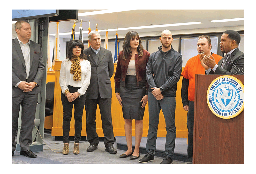 Aurora mayor Richard Irvin gives a salute to community members at Tuesday’s media briefing who offered help in Friday’s shooting. Jeff Hartman, left, is from Community Foundation of the Fox River Valley; Aurora Noon Rotary representives Linda Kemp and Charlie Zine; Sarah Cervantes, Seven Brighter, and Chad Jimenez from the city government of Aurora who created Aurora Strong apparel; and Bob Lockwood, manager of Luigi’s Pizza, which donated meals to first responders. Jason Crane/The Voice