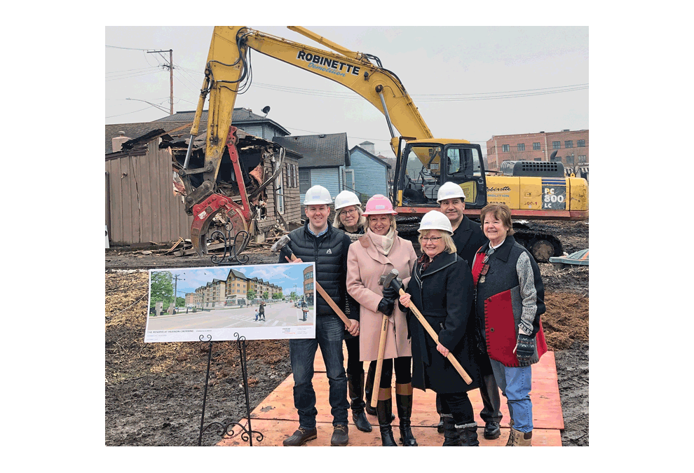 Oswego Village Board trustees Ryan Kauffman and Judy Sollinger, Village president Gail Johnson, and trustees Karin McCarthy Lange, Luiz Perez, and Pam Parr celebrate at the project kick off for The Reserve at Hudson Crossing, on the site of the former Alexander Lumber yard in downtown Oswego Wednesday, Feb. 6. In the foreground, a poster shows a rendering of the future project.