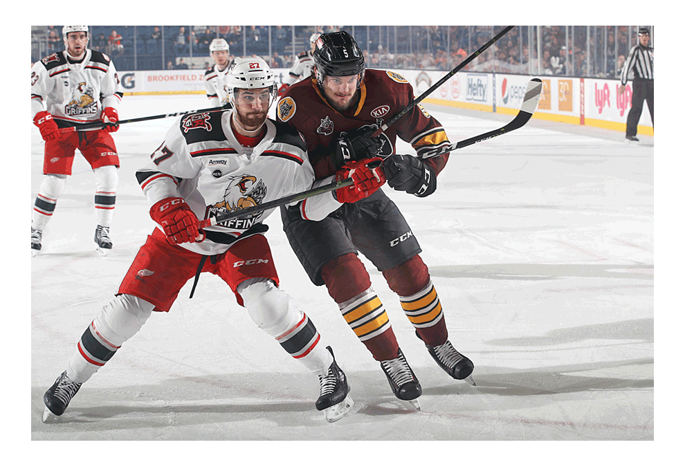 Jake Chelios, left, of Grand Rapids, and Tye McGinn of the Chicago Wolves, jostle for position in Saturday's second playoff game. The Wolves won, 3-2, after faltering, 5-1, in game one. Both games were played in Rosemont at the Allstate Arena. Game five, if necessary would be at 3 p.m. Sunday in Rosemont. Jake Chelios is the son of Chris Chelios, National Hockey League Hall of Fame player. Ross Dettman/Chicago Wolves