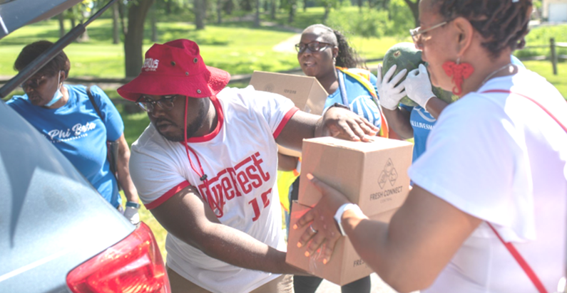 Black fraternities and sororities place food boxes into trunks of vehicles at a previous Juneteenth Food Distribution.