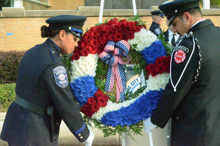 Photo of an Aurora police officer and a firefighter team up to place a wreath during the 9/11 remembrance ceremony outside Aurora Police Department on Wednesday, Sept. 11.. The ceremony commemorates the 23rd anniversary of the terrorist attacks on Sept. 11, 2001.